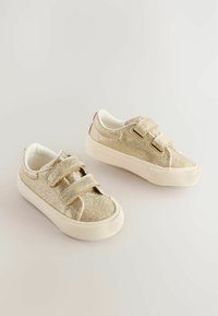 Des baskets dorées scintillantes avec deux sangles Velcro réglables, des semelles en caoutchouc blanches et une doublure interne douce. Texture lisse et forme arrondie.