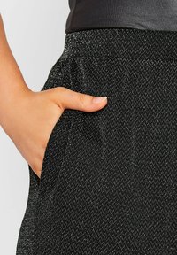 Svarta byxor med ett texturerat mönster och silvertrådar. Har en sidoficka och elastisk midja. Slät tyg med subtil lyster.