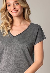 Haut gris métallique à manches courtes avec un décolleté en V. Présente une texture lisse et un léger éclat, mettant en avant une coupe décontractée.