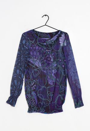 Blusa trasparente a maniche lunghe in viola con intricate fantasie di cuori e foglie blu e verdi. Presenta un orlo arricciato e una chiusura a bottoni sul retro.
