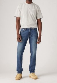 Grå bomullströja med korta ärmar, blå denimjeans och beige mokasiner. Rak passform och minimal branding på tröjan.