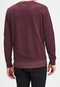 Bordeauxrode crewneck trui met lange mouwen, geribbelde manchetten en zoom. Gladde stoftextuur, eenvoudig ontwerp zonder patronen of accenten.