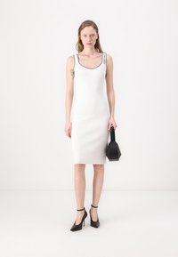 Balta pieguļošā kleita ar apaļu dekoltē un melnu apdari. Savairota ar melniem augstiem papēžiem un ģeometrisku melnu rokassomu.