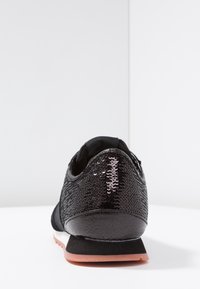 Svart sneaks i paljettmaterial, med rund tå, låg profil och en kontrasterande rosa gummisula. Slätt, glänsande material.