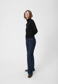 Black long-sleeve turtleneck top paired with dark blue flared jeans and brown suede shoes, showcasing a casual, fitted silhouette.