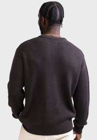Mørkebrun strikket sweater med en tekstureret ribbet mønster, lange ærmer og rund halsudskæring. Kantene er let elastiske.