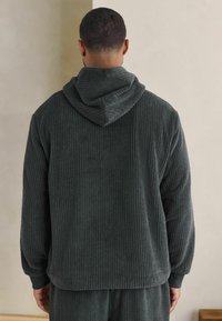 Felpa con cappuccio grigio scuro, dal texture a costine, con vestibilità ampia e maniche lunghe. Materiale morbido con design semplice e polsini elastici.