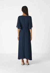 Marinblå maxiklänning med fyrkantig halsringning, korta volangärmar, elastisk midja och genomskinlig tyg. Faller till anklarna med minimalt med detaljer.