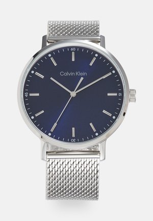 Silver mesh bracelet watch with a round navy blue dial, silver hour markers, and hands. Features a textured band and a minimalist design.