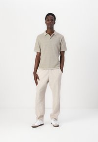 Hele halli tekstuuriga polo särk koos kraega, millele on sobitatud beežid vabalt istuvad püksid. Komplekti täiendab valgeid spordijalatsid. Minimalistlik disain.