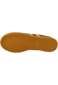 Ruskea lenkkari, jossa on keltaisia raitoja, kumipohja, jossa on kalanruoto kuvio, ja logo sivussa. Kestävä materiaali ja rento muotoilu.