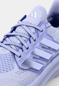 Närbild av en ljuslila mesh sportskor med reflekterande tre-stripes-logotyp och korsade snören på vit bakgrund.