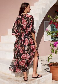 Svart blommig kimonoklänning med rosa rosor, genomskinligt tyg, lösa ärmar och knyt i midjan, med en slits högt upp på låret, bärs med svarta sandaler.