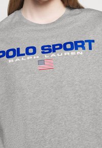 Šedé bavlněné tričko s výrazným modrým nápisem "POLO SPORT", bílým nápisem "RALPH LAUREN" a malou grafikou americké vlajky.