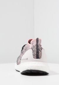 Růžová a černá pletená běžecká obuv s bílou podrážkou, zobrazena ze zadní strany, na které je vidět značka "ultraboost" na patě.