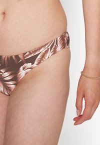 Parte de baixo de biquíni castanho com um padrão de folhas tropicais em rosa e branco, apresentando um corte de cintura baixa e detalhes franzidos nas laterais.