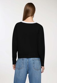 Pullover nero con una vestibilità rilassata, scollatura ampia e maniche lunghe, abbinato a jeans in denim chiaro con due tasche posteriori.