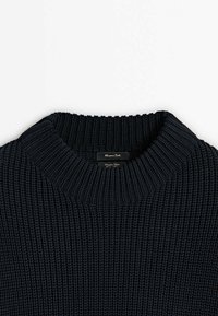 Gros plan d'un pull en maille épaisse noire avec col rond côtelé et étiquette de marque visible à l'intérieur du col.