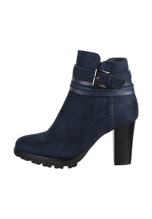 Botines de ante azul marino con una correa texturizada que cuenta con acentos metálicos y un alto tacón cuadrado. Incluye una suela de goma con taqueado.