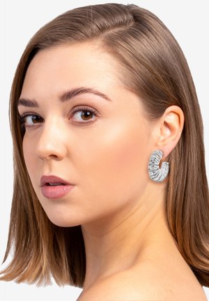 Silver hoop earring with a twisted, textured design, featuring a shiny finish. Model showcases the earring in a side profile.