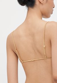 Gold satin triangle bralette with narrow adjustable straps and a clasp closure at the back, featuring smooth texture and minimal design.