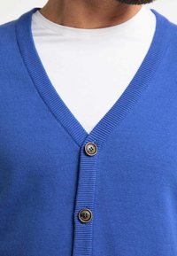 Blå cardigan i mjukt material, med djup V-ringning, ribbat kantband och två mörkbruna knappar fram.