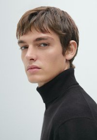 Maglione nero a collo alto realizzato in materiale morbido, con un design aderente, visto di lato su una persona.