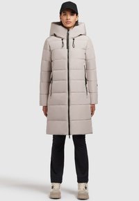 Manteau rembourré gris clair avec capuche, doté d'une fermeture éclair à l'avant et de détails noirs. Il a une coupe décontractée et des poches latérales. Associé avec un pantalon noir.