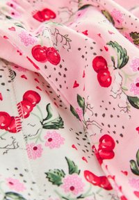 Rosa Stoff mit Kirschen, Blumen und kleinen Herzen. Das Design umfasst grüne Blätter und schwarze Punkte sowie eine weiche Textur.