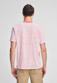 Röd och vit randig t-shirt med korta ärmar och rund hals, tillverkad av mjukt bomullsmaterial, med en rak fåll och avslappnad passform.