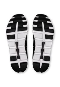 Fekete-fehér atlétikai cipőtalpak texturált gumimintázattal, kifejezett futófelületi mintával és látható márkajelzéssel az oldalakon.