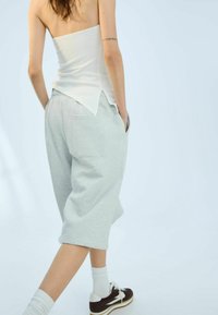 Šedé teplákové šortky s bočními kapsami, zkombinované s bílým přiléhavým topem s špičatým zadním lemem. Model má na sobě bílé ponožky a tmavé tenisky.