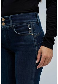 Jeans de mezclilla azul oscuro con un diseño de cintura alta, que presentan dos botones frontales, una tela texturizada y un detalle de herraje en el lateral.