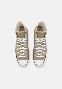 Una coppia di scarpe da ginnastica alte in tela beige con lacci bianchi e punte in gomma su uno sfondo bianco.