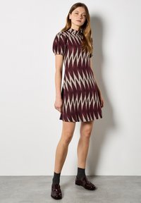 Robe à manches courtes et col haut présentant un motif en zigzag en bordeaux et crème, avec un corsage ajusté et une jupe évasée.