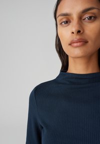 Dunkelblaues, geripptes Langarmoberteil mit hohem Halsausschnitt. Es zeichnet sich durch ein enganliegendes Design und eine glatte Textur aus, die eine minimalistische Ästhetik zur Schau stellt.