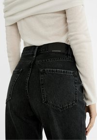 Jeans negros de cintura alta con un diseño ajustado, que presentan bolsillos traseros y una etiqueta de cuero negra en la cinturilla. Tejido denim texturizado.