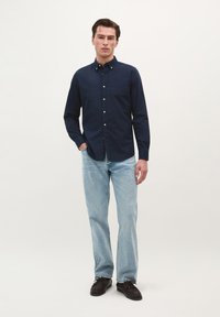 Marineblaues Hemd mit Knopfverschluss und Brusttasche, kombiniert mit hellblauen Jeans und dunklen Schuhen. Baumwollstruktur, lange Ärmel, klassisches Design.