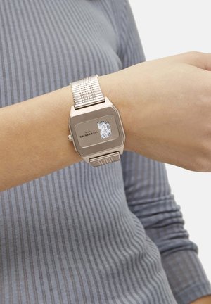 Montre rectangulaire en argent avec un bracelet en maille, dotée d'un écran digital blanc affichant l'heure et des détails de marque sur le cadran.