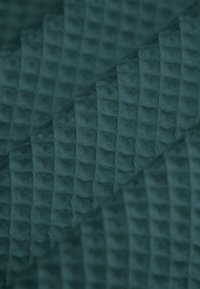 Strukturierter Stoff in dunklem Petrol mit einem erhöhten karierten Muster, weicher Textur und einer geschichteten Optik.