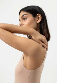 Ihonvärinen hihaton bodysuit, jossa on sileä pinta, leveä olkaimet ja tiukka muoto, joka korostaa ihonväriä.