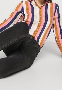 Randig skjorta med knappar i rosa, orange, marinblå och vit; matchad med svarta tajta jeans. Mjuk tyg med långa ärmar och klassisk krage.