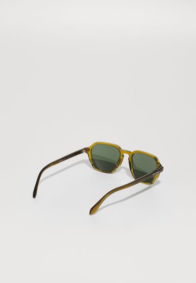 Ochelari de soare hexagonali cu lentile verzi, ramă transparentă cu nuanțe de galben și brațe cu model maroniu. Design ușor, cu margini elegante.