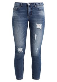 Jeans ajustados azules con parches desgastados en los muslos y las rodillas, que cuentan con bolsillos frontales, ansa para cinturón y un cierre de botón.