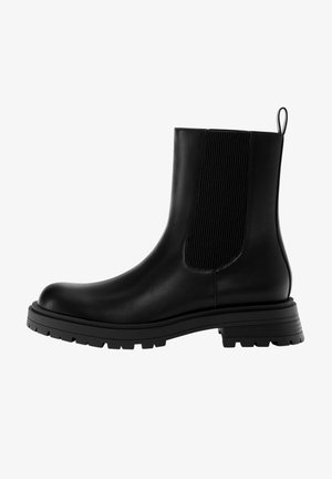 Musta nahkainen nilkkasaapas, jossa on paksu pohja, joustavat sivupaneelit ja vetoluuppi. Ominaisuuksinaan sileä pinta ja kestävä muotoilu.