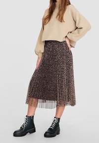 Sudadera recortada beige, falda midi de leopardo semitransparente con pliegues, botas de tobillo negras con cordones y suelas gruesas. Detalles de tela texturizada visibles.