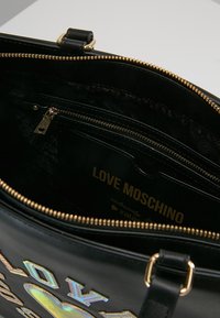 Zwarte leren handtas met gouden ritssluiting, voorzien van een getextureerde binnenkant en een bedrukt "LOVE MOSCHINO" label. Kleurrijke geborduurde letters aan de voorkant.
