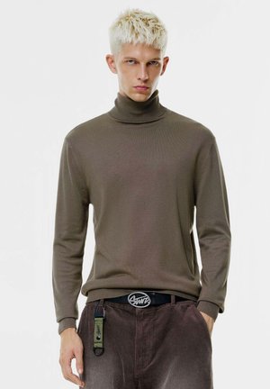 Maglione a collo alto marrone in morbido tessuto a maglia, con maniche lunghe e taglio slim. Abbinato a pantaloni di velluto a coste marroni e una cintura nera.