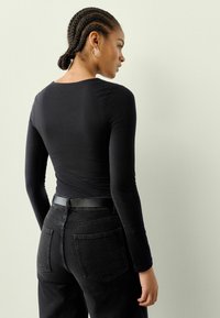 Melnas garām piedurknēm topiņš izgatavots no mīkstas auduma, apvienots ar augsto jostasvietu melniem džinsiem, kas aprīkoti ar ādas jostu un aizmugurējām kabatām.