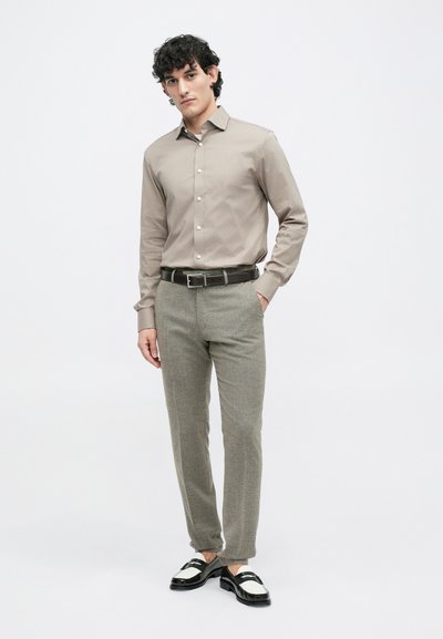 Light beige long-sleeve shirt with buttons, tailored grey textured trousers, and black-and-white shoes with a strap detail, set against a plain background.